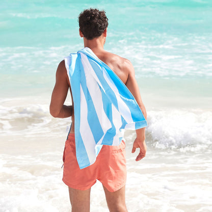 man with light blue striped microfiber beach towel on the beach, designed to be quick dry, sand free, lightweight, and easy to pack