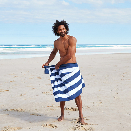 man on beach wrapped in absorbent navy striped beach towel on a sandy beach