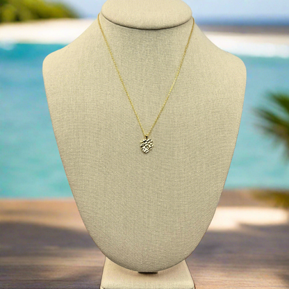 monstera tropical leaf pendant necklace 18k gold dipped necklace is perfect jewelry accessory for beach lovers on linen jewelry display with an ocean background