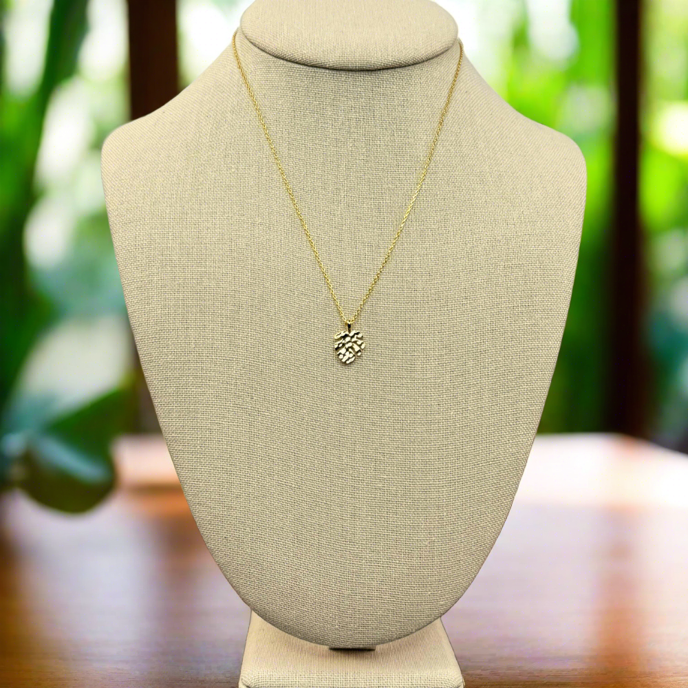 monstera tropical leaf pendant necklace 18k gold dipped necklace is perfect jewelry accessory for beach lovers on linen jewelry display in a tropical setting