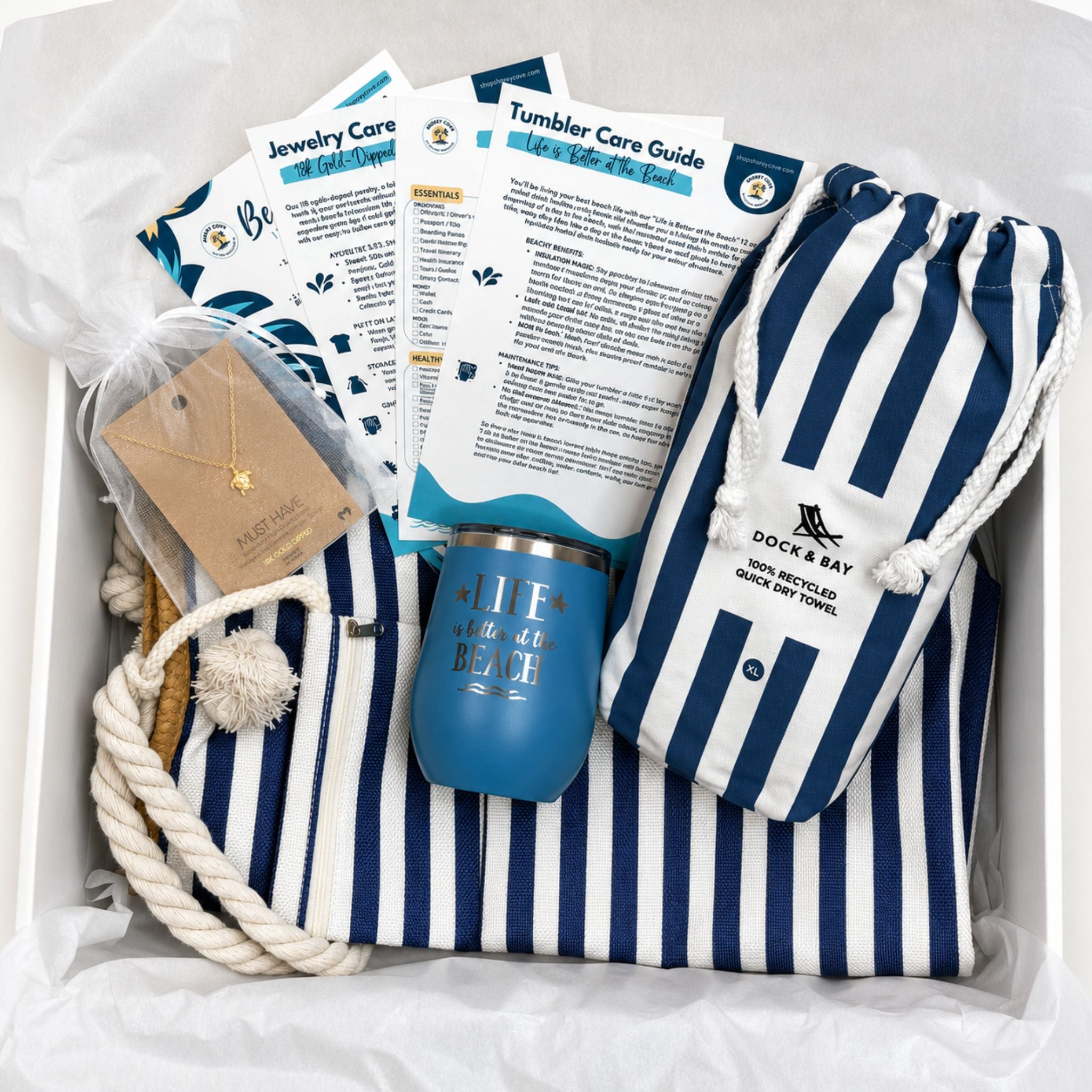 Ready-to-gift navy beach gift set arranged in a box with a striped beach bag, towel, ocean blue tumbler, care cards, and sea turtle necklace in an organza bag.