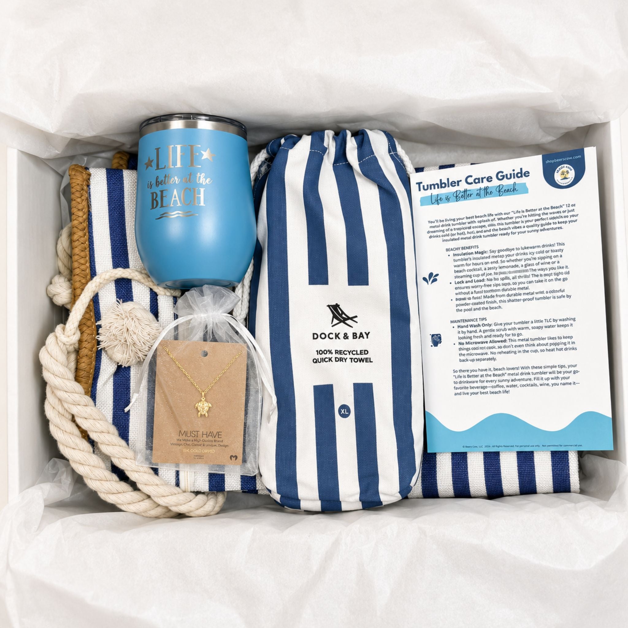 Navy beach gift set packaged in a gift box with a striped beach bag, towel, ocean blue tumbler, sea turtle necklace, and care guide for beach lovers.