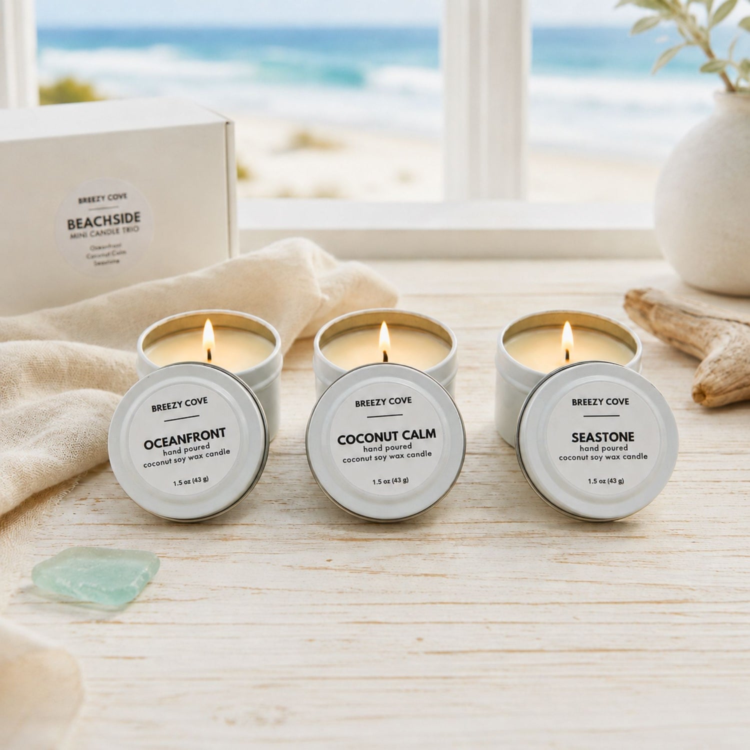 Three lit clean burning nontoxic beach candles from the Beachside Mini Candle Trio on a white coastal table with the gift box behind them.