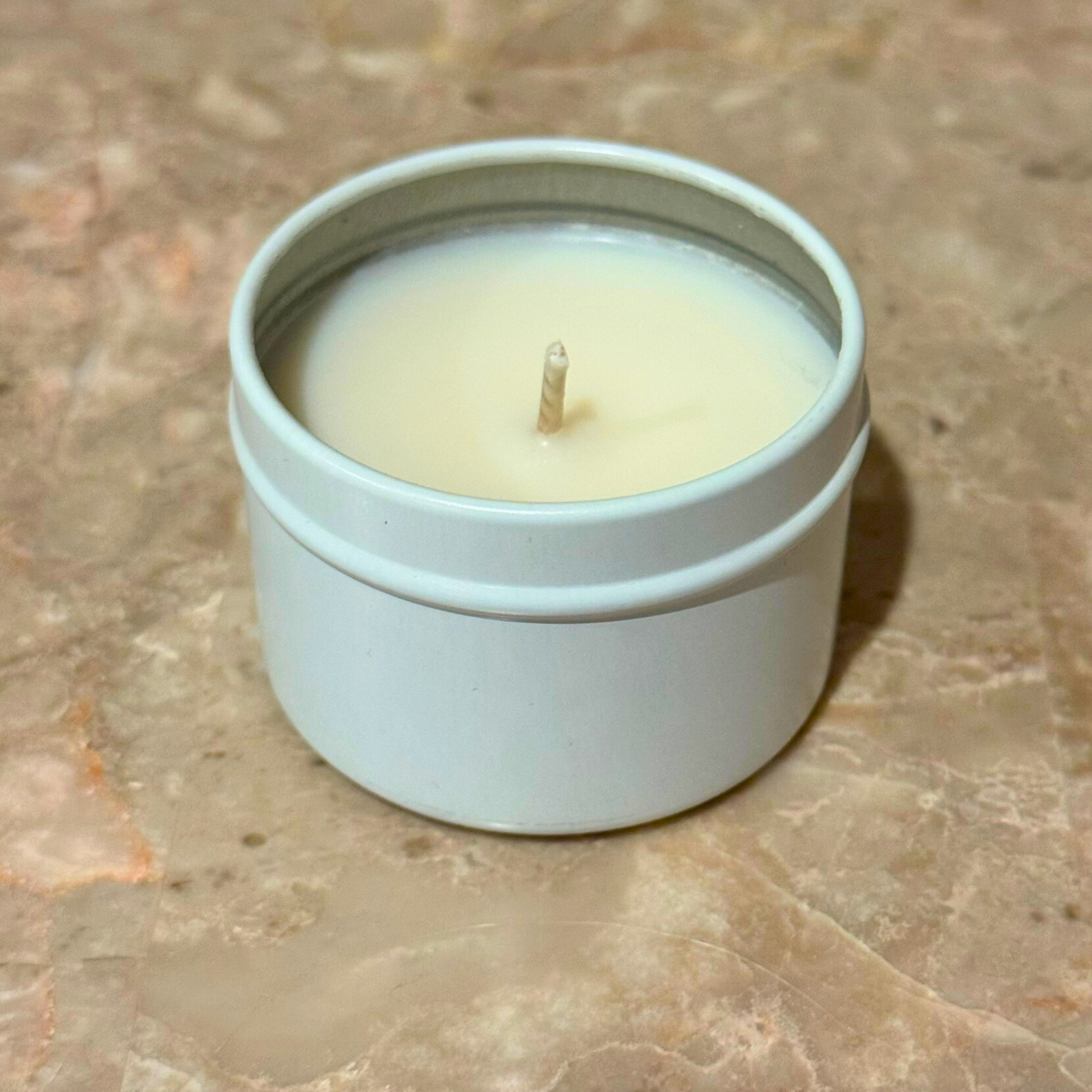 Single nontoxic long-burning beach candle in a white tin on a marble surface.