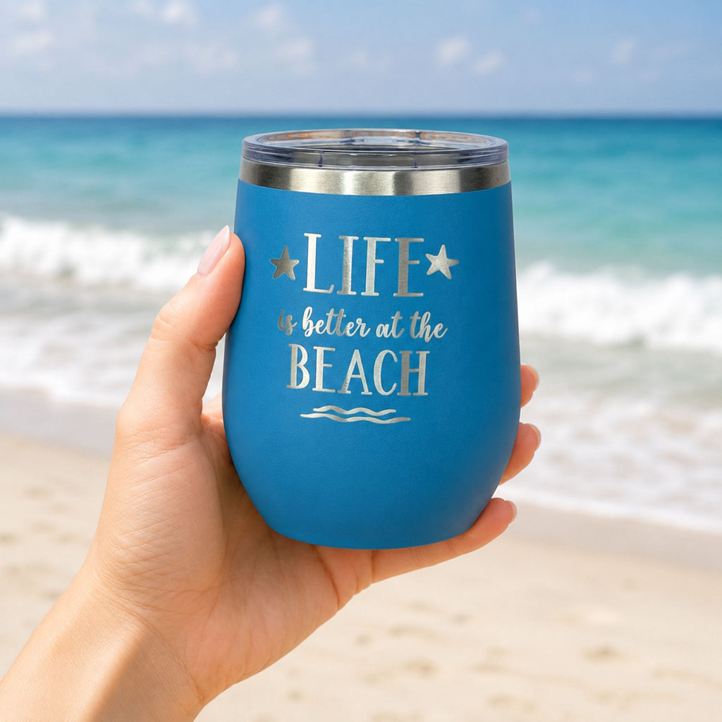 Hand holding ocean blue beach wine tumbler with lid in front of the ocean