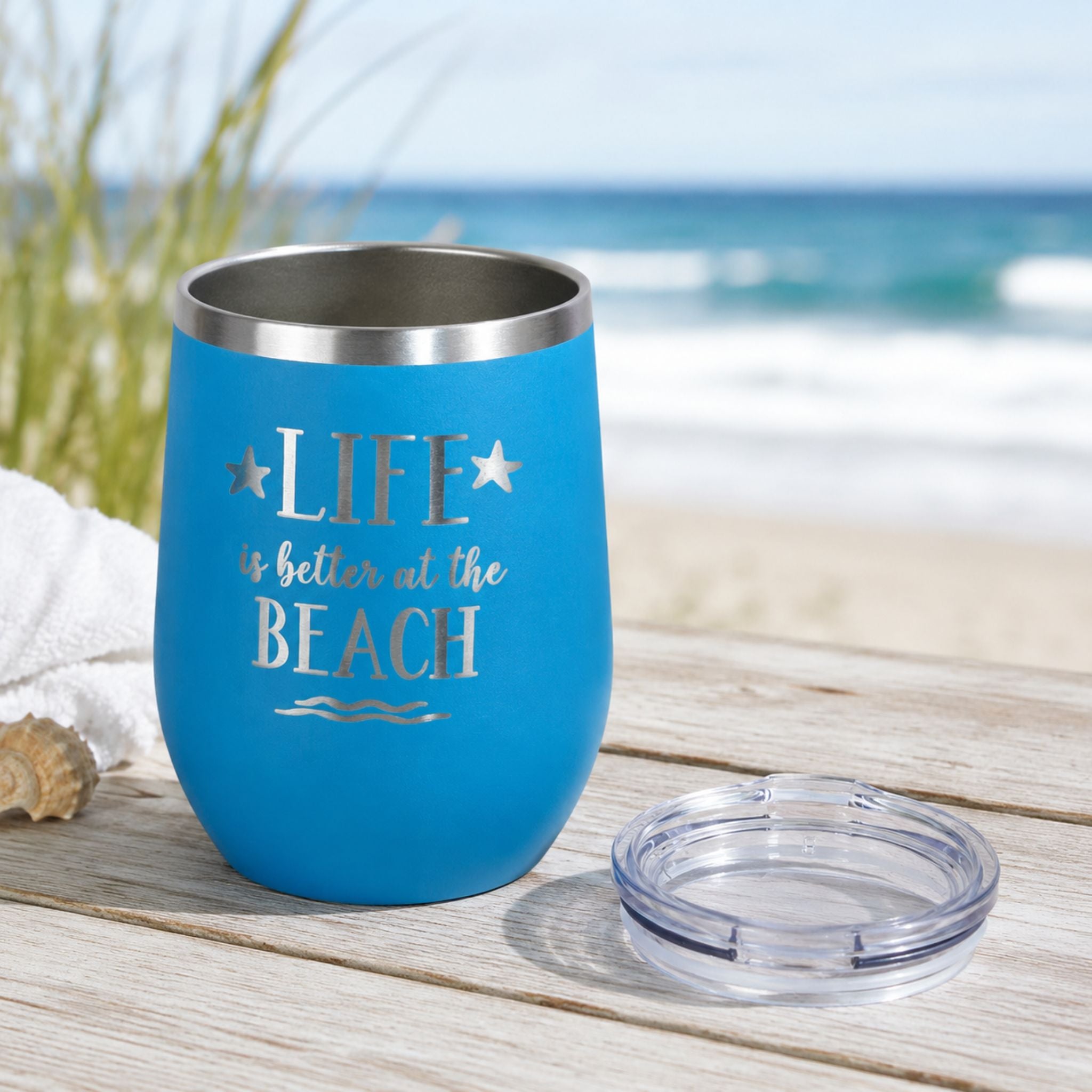 Ocean blue wine tumbler with clear lid shown beside the cup on a coastal wood surface