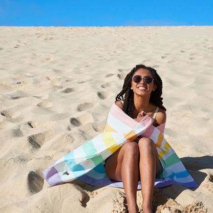 Pastel striped microfiber beach towel on the beach, designed to be quick dry, sand free, lightweight, and easy to pack