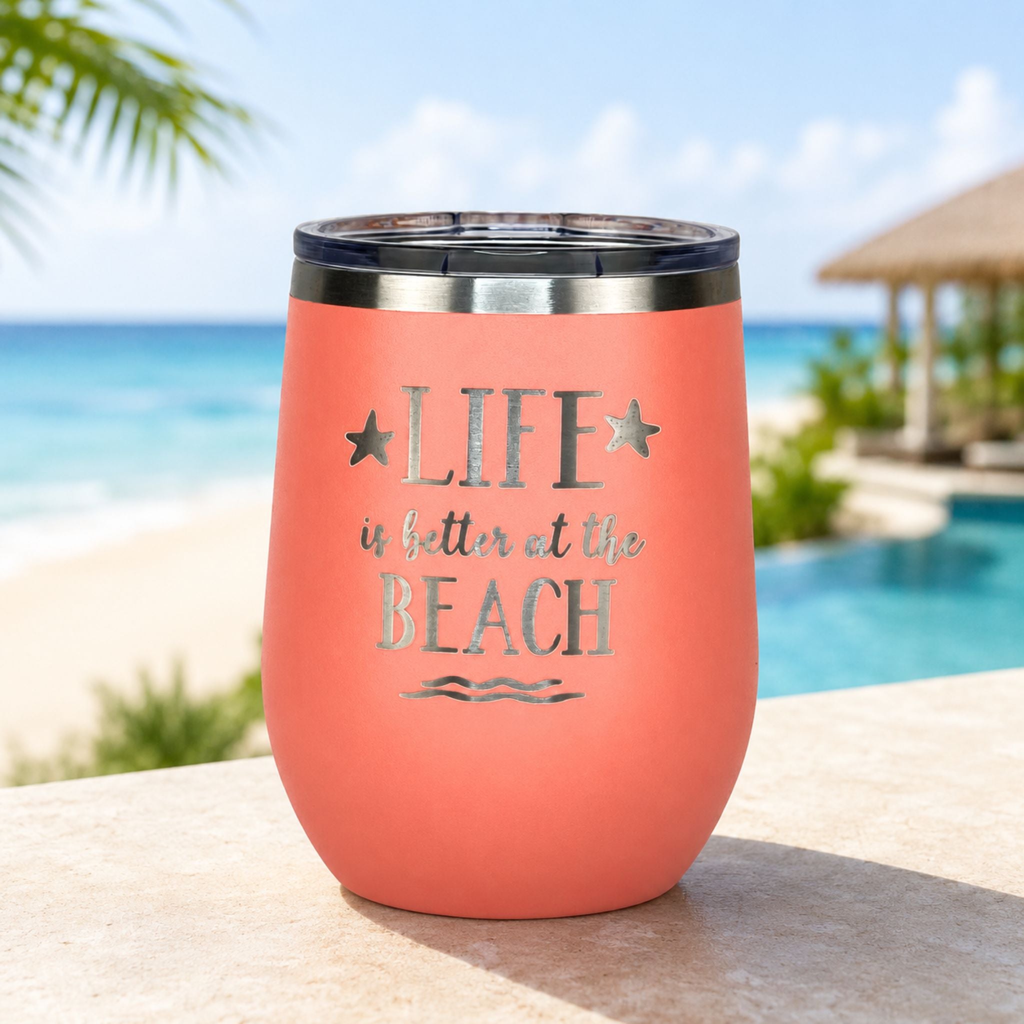 peach metal tumbler with 'Life is better at the Beach' text by a poolside with palm trees and an ocean view as a beach gift for women