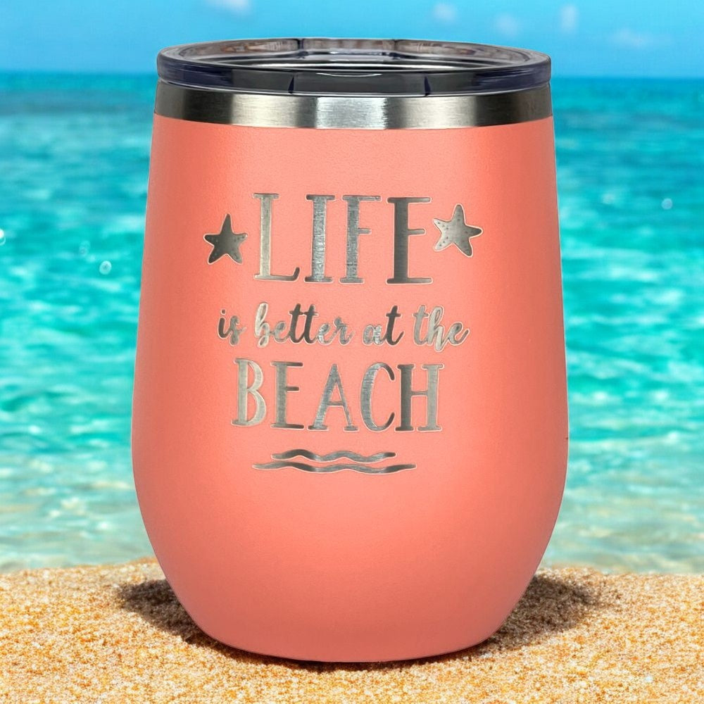 Peach "Life is Better at the Beach" insulated tumbler with lid on a sandy beach.