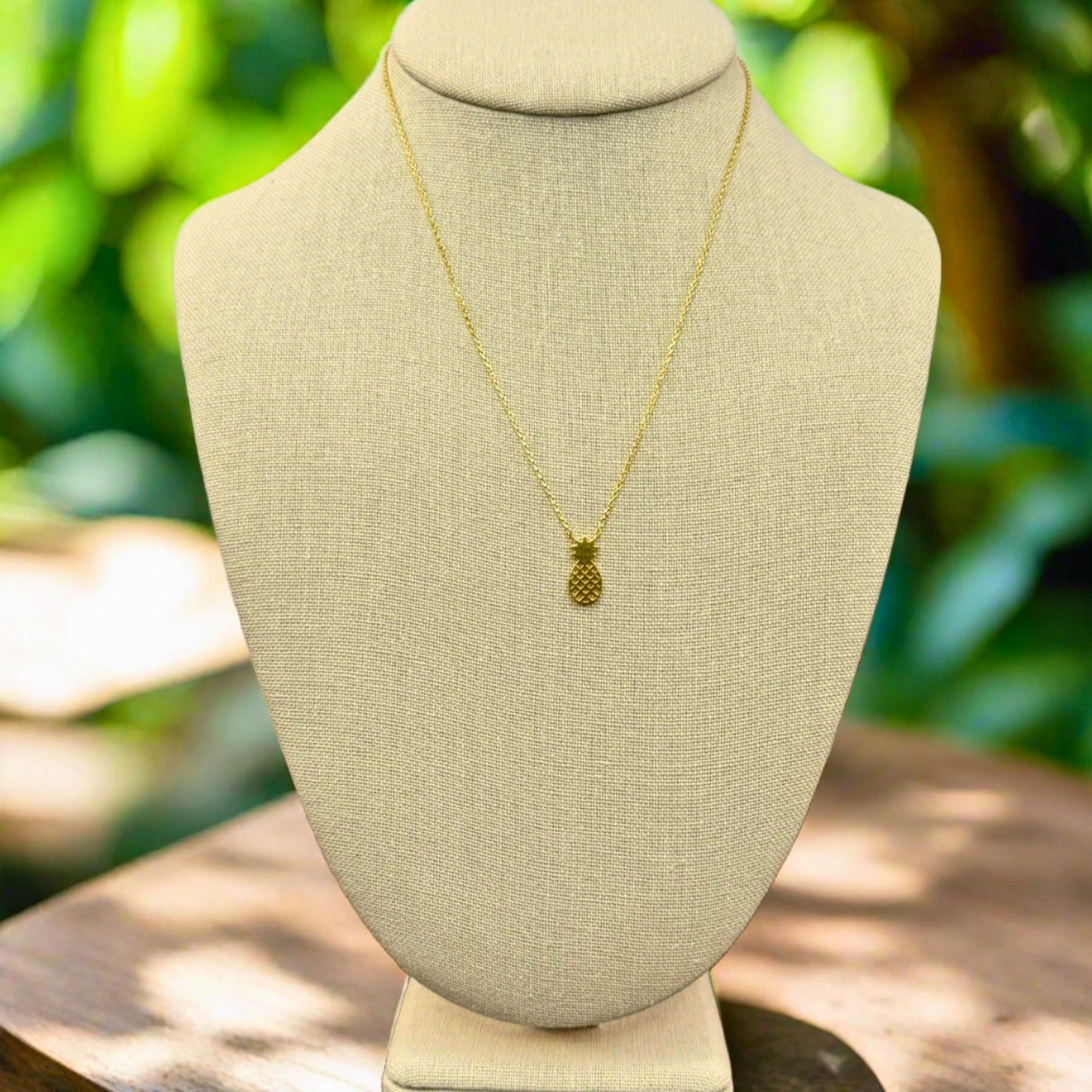 Gold pineapple beach inspired necklace on a beige mannequin bust with a natural background