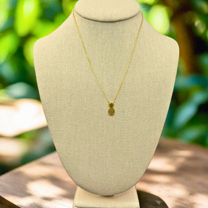 Gold pineapple beach inspired necklace on a beige mannequin bust with a natural background