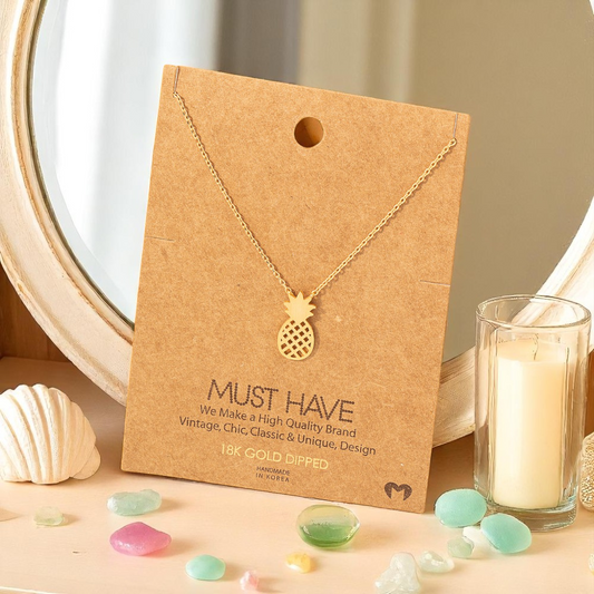 Dainty gold pineapple necklace styled on a beach vanity to evoke sunshine and calm.
