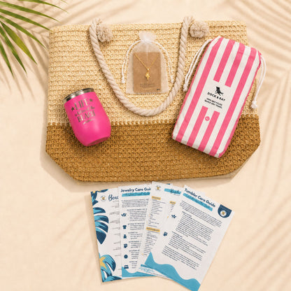Pink beach lover gift set flat lay with straw beach bag, pink striped quick-dry towel, pink Life Is Better at the Beach tumbler, conch shell necklace in a white organza bag, and beach-themed care cards.