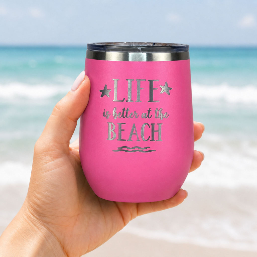 Hand holding pink beach wine tumbler with lid in front of the ocean