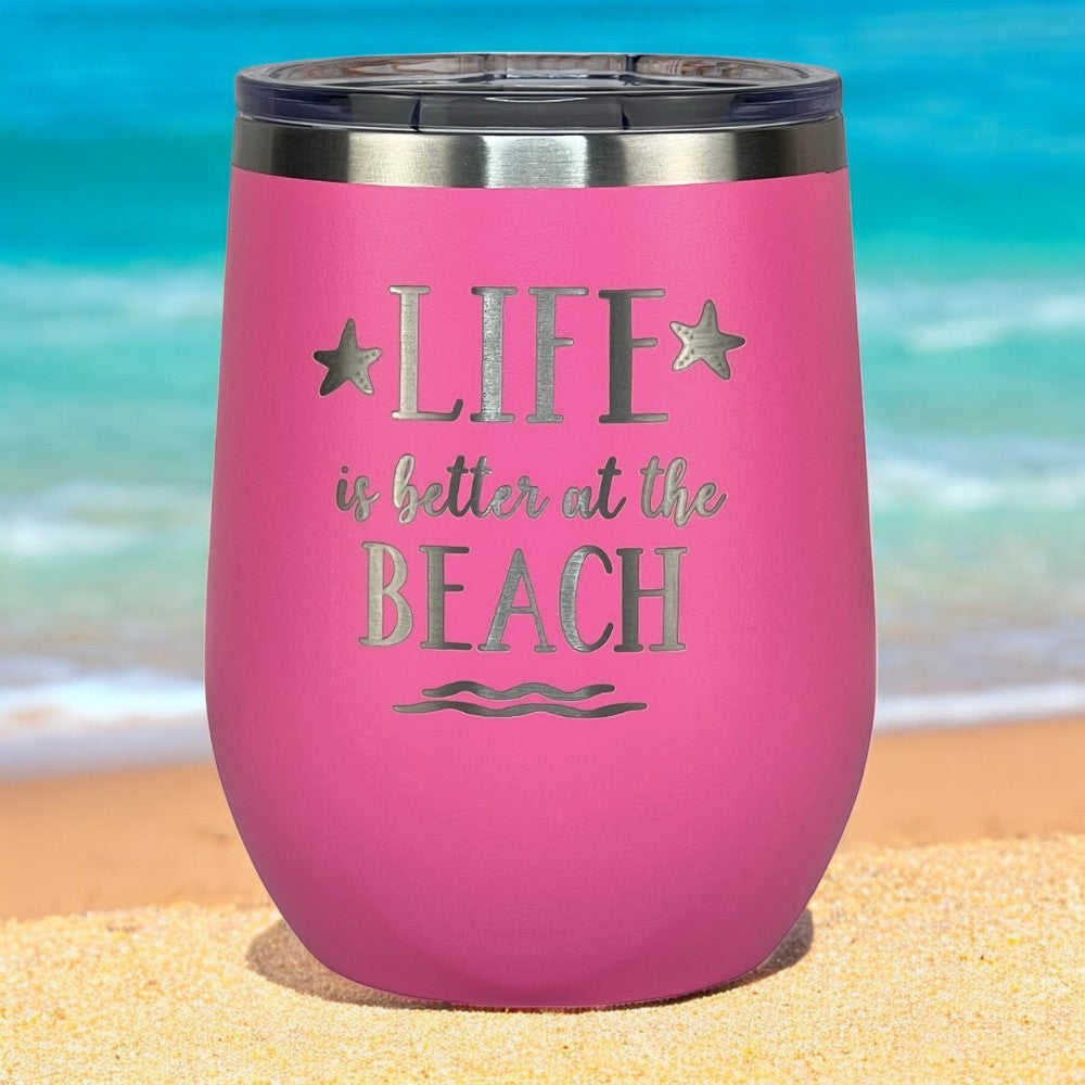 Pink insulated tumbler with lid on a sandy beach, perfect for summer drinks