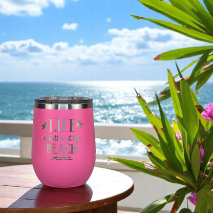 pink insulated wine tumbler on a wooden table near a tropical palm with ocean view