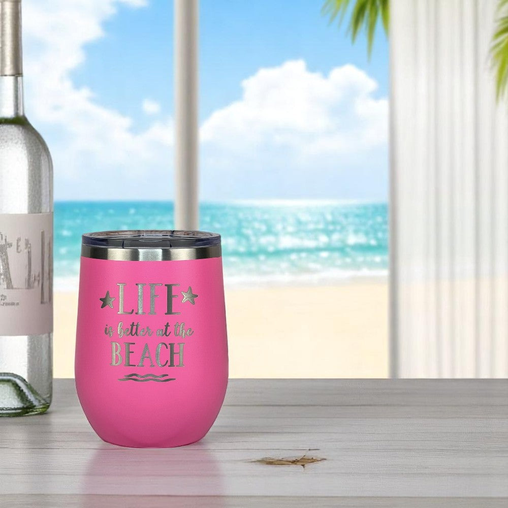 pink wine tumbler on a light wood table near a wine bottle and an ocean view from the patio