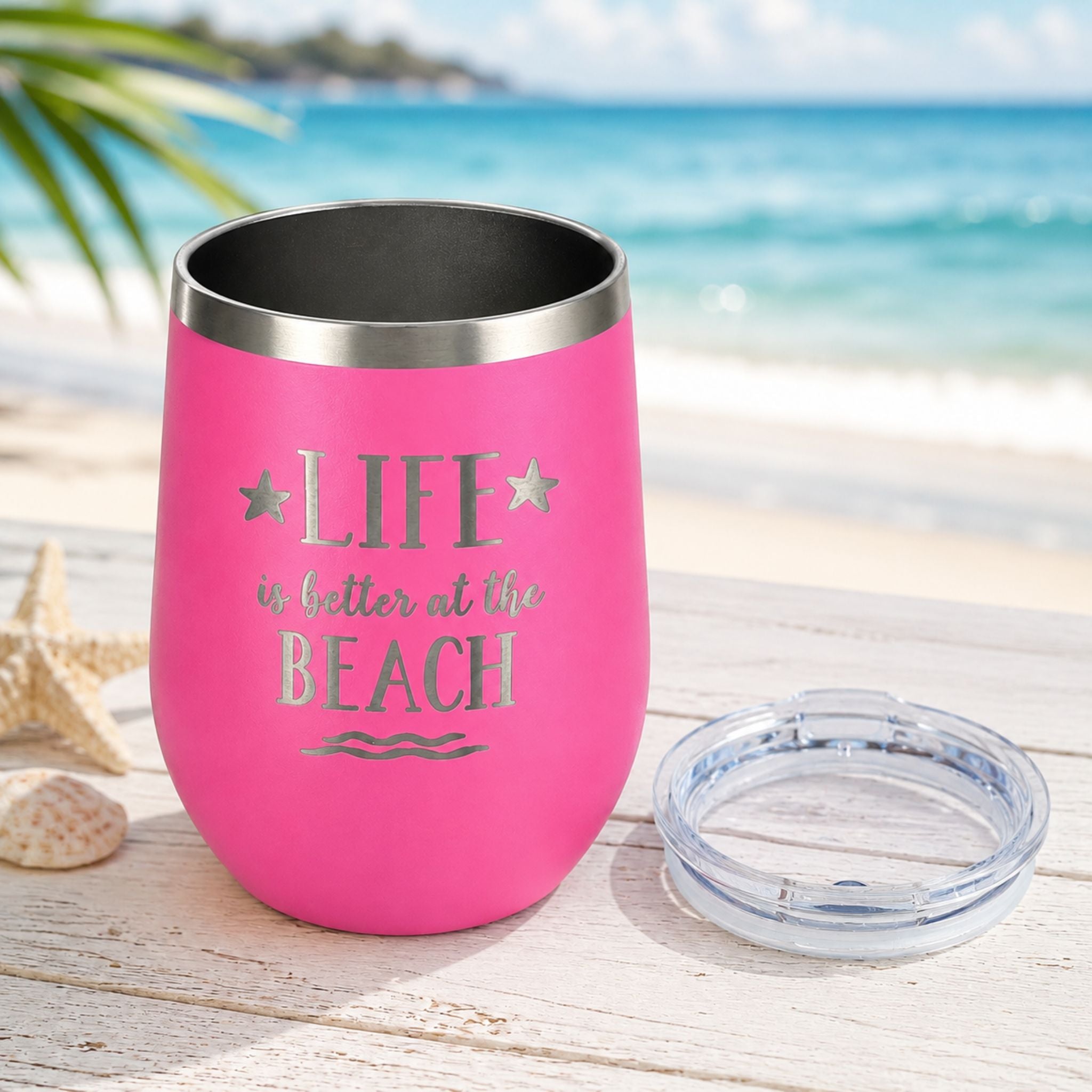 Pink wine tumbler with clear lid shown beside the cup in a beach-inspired setting