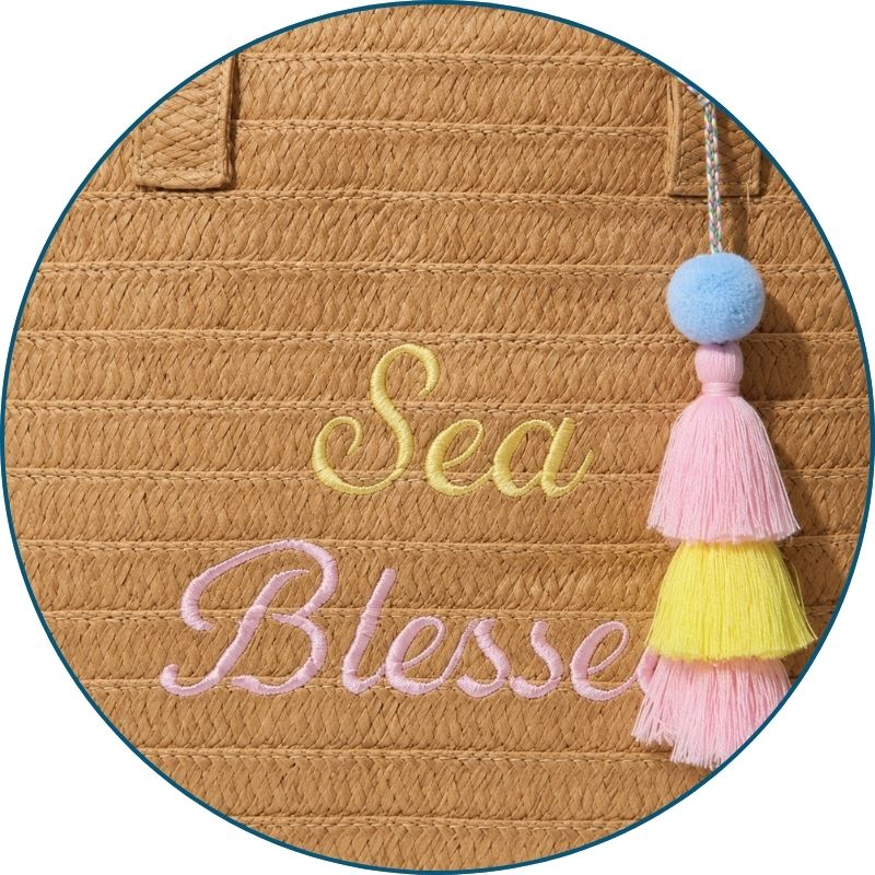 Colorful Sea Blessed embroidery and removable bag charm tassel on a woven raffia tote bag