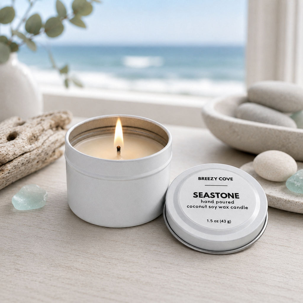 Lit Seastone beach candle in a calm coastal setting with smooth stones, sea glass, and an ocean view.