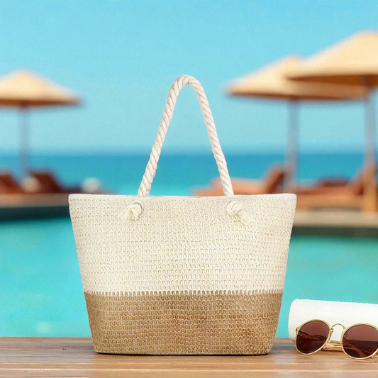 Neutral straw beach bag beside white towel and gold sunglasses on sunny dock with clear turquoise ocean and cabanas in the background in a beach setting.