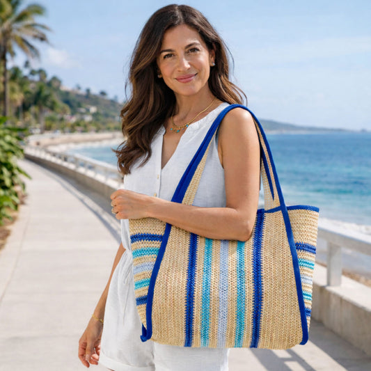 Woman holding a blue striped straw tote bag by the beach
