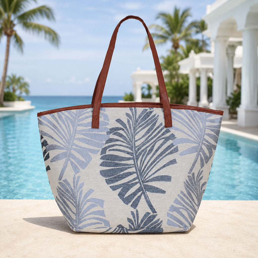Tropical leaf patterned tote bag with brown handles by a poolside.