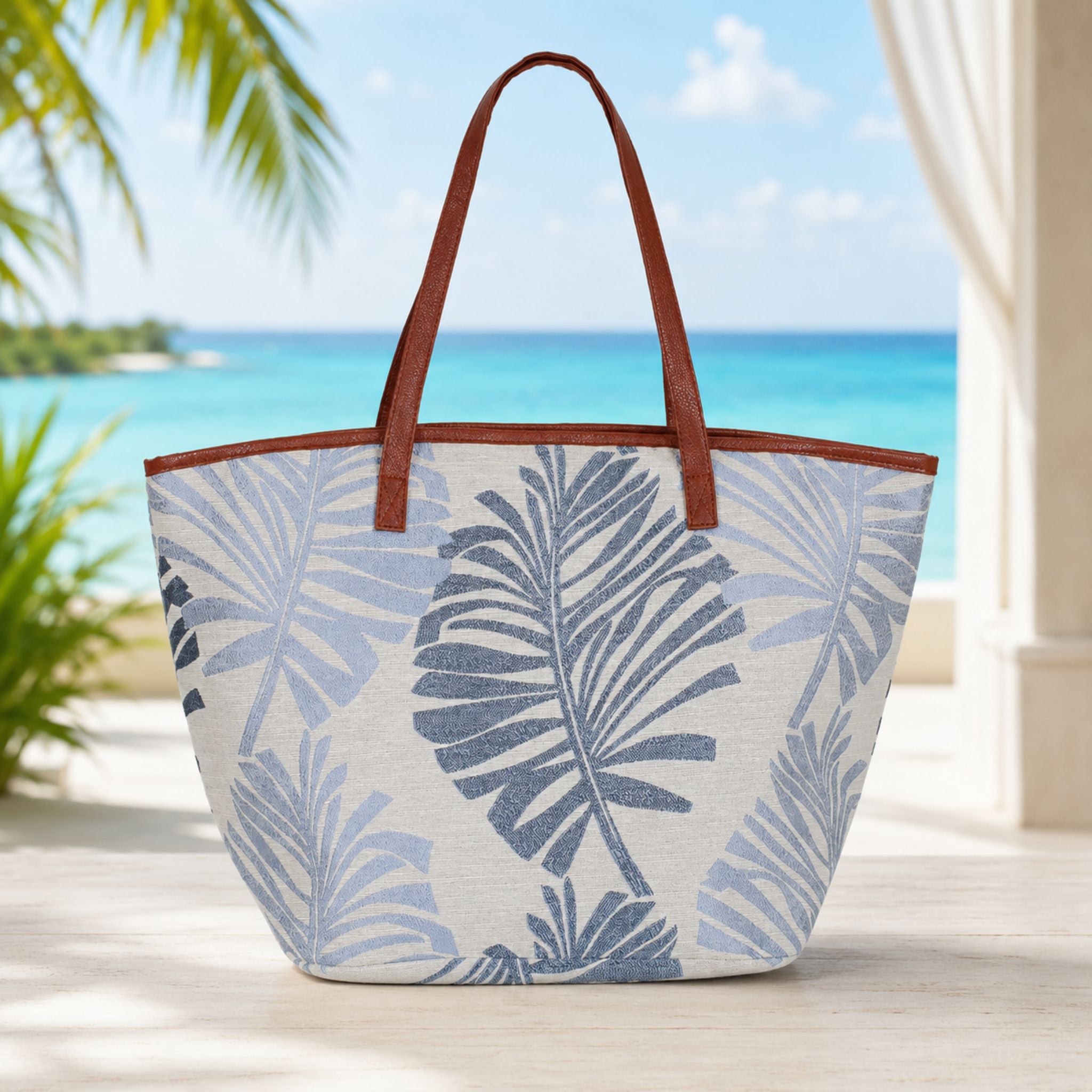Tropical leaf patterned tote bag with brown handles on a beach setting