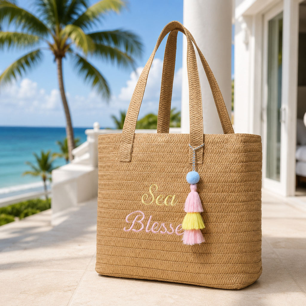 Sea Blessed woven raffia tote bag on a sunny resort terrace with an ocean view