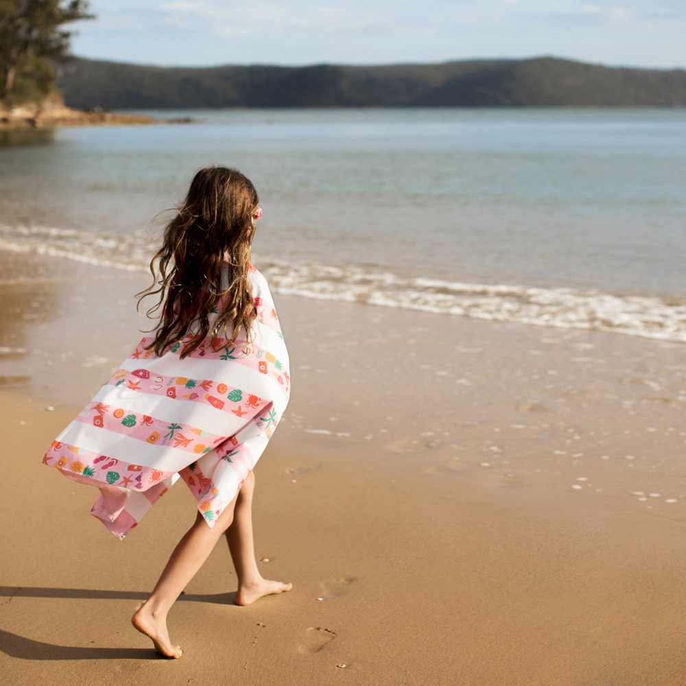 girl on sandy beach wrapped in pink striped beach pattern, quick dry, sand free kids beach towel