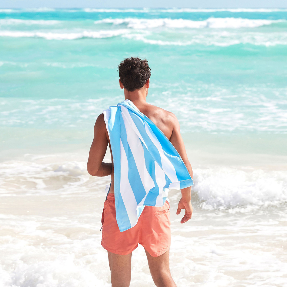 man on beach with light blue, quick dry striped beach towel over should